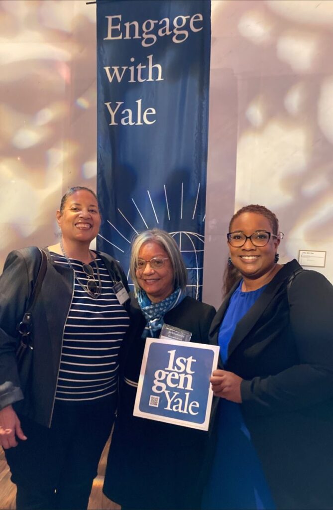 Three alums hold a 1stGenYale sign and stand underneath a banner that says Engage with Yale