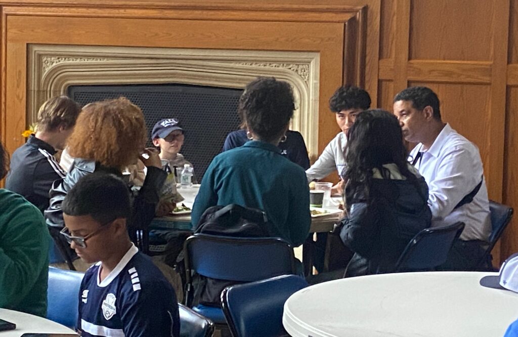 A group of adults and children sit around a table and talk
