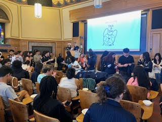 Students and alums sit, stand, and talk in a room with a screen projecting a drawing of a bulldog